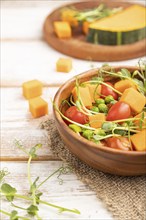 Vegetarian vegetable salad of tomatoes, pumpkin, microgreen pea sprouts on white wooden background