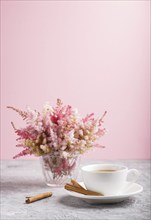 Pink and red astilbe flowers in glass and a cup of coffee on a gray and pink background. Morninig,