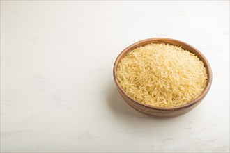 Wooden bowl with raw golden rice. Side view, close up, copy space