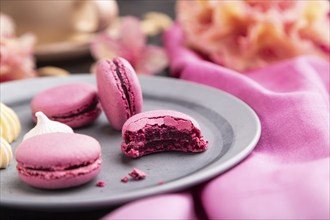 Purple macarons or macaroons cakes with cup of coffee on a black concrete background and pink