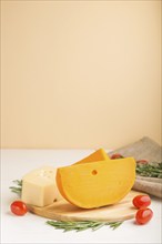 Various types of cheese with rosemary and tomatoes on wooden board on a white and orange background