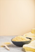 Blue ceramic bowl with raw golden rice and wooden spoon on a gray and orange background and yellow