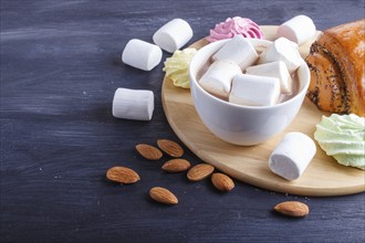 A cup of hot chocolate with marshmallow, bun and meringues on black wooden background. close up,