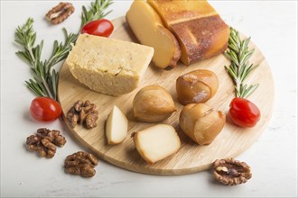 Smoked cheese and various types of cheese with rosemary and tomatoes on wooden board on a white