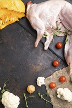 Whole raw rabbit with pumpkin, tomatoes, pea sprouts on a black concrete background and linen