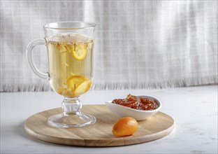 Jasmine tea with kumquat in a glass cup on a wooden board on a white background. close up, copy