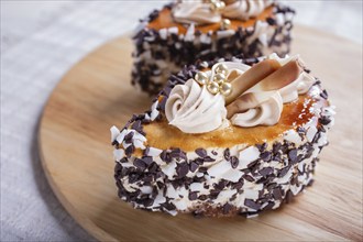 Cakes with chocolate chips and cream decorations on wooden board on white background. selective