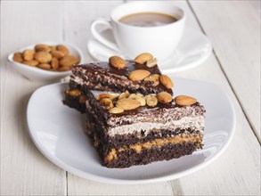 Chocolate cake with caramel, peanuts and almonds on a white wooden background. cup of coffee, top