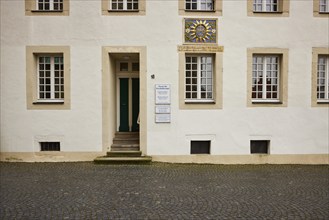 Façade of a historic building with white windows and a colourful family coat of arms in the old