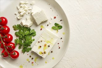 Feta cheese, for salads, with cherry, green butter, greens, on a white plate, appetizer, top view,