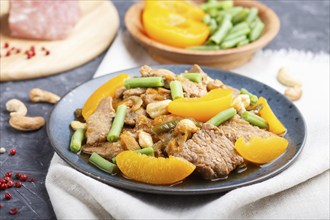 Fried pork with peaches, cashew and green beans on a black concrete background. Side view, close