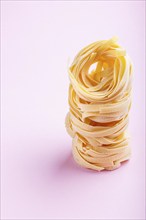 Raw uncooked tagliatelle pasta on a pink pastel background. side view, close up, copy space