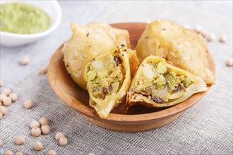 Traditional indian food samosa in wooden plate with mint chutney on a gray concrete background.