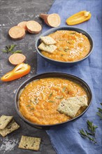 Sweet potato or batata cream soup with sesame seeds and snacks in blue ceramic bowls on a black