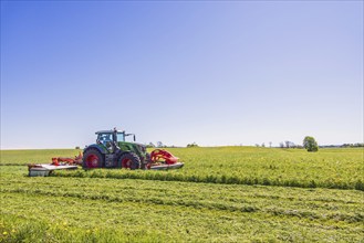 Tractor harvesting grass on a large field in the countryside on a sunny summer day