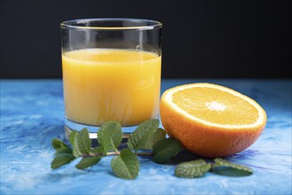 Glass of orange juice with mint on a black and blue background. Hard light, contrast. Side view,