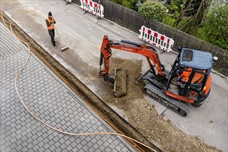 Construction workers lay fibre optic cable in trench under asphalt, cable trench, excavator,