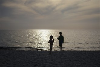 Siblings stand on the beach against the light of the setting sun. Born, 01.08.2024