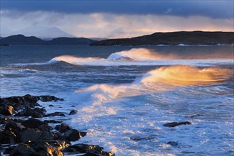 Large waves crash in a winter storm and the swirling spray is illuminated by the warm light of the