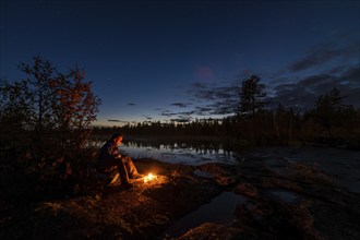 Man in the evening at a bivouac with campfire, Lapland, Sweden, Scandinavia, Europe