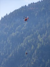 Injured person in a mountain bag with an air rescuer being winched into the rescue helicopter