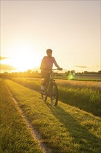 A cyclist rides on a dirt track through the natural landscape at sunset, Gechingen, Black Forest,