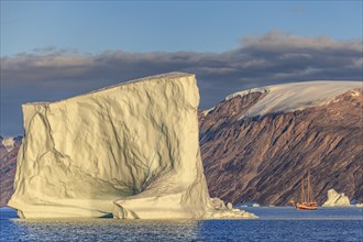 Sailing boat, ship in fjord in front of large icebergs and mountains, evening light, Scoresby