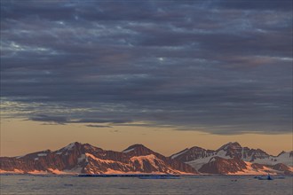 Evening light and atmosphere in fjord with icebergs in front of steep mountains, cloudy, autumn,