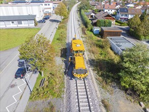 Yellow maintenance vehicle on the railway tracks near a road and residential buildings under a