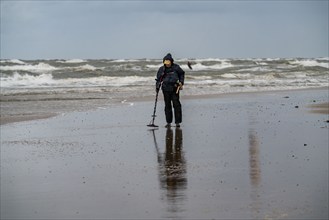 Treasure hunter, man with metal detector on the beach, dark storm clouds, autumn at the North Sea