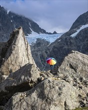 Woman with colorful open umbrella between large rocks, glacier Lenangsbreen, at glacier lake