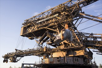 A man swings in front of an open-cast mining excavator illuminated by the evening sun at the Melt