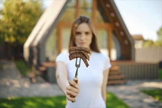 Defocused young woman stretching forward a barbecue fork with slices of steak in her hand