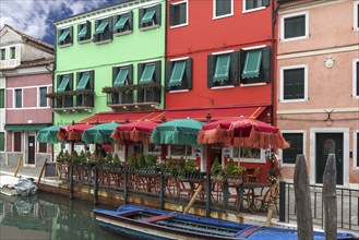 Colourful houses and colourful parasols in a restaurant on the canal, Burano, Venice, Veneto,