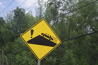 Yellow warning sign with a car driving on a slippery slope surrounded by trees, Quebec, Canada,