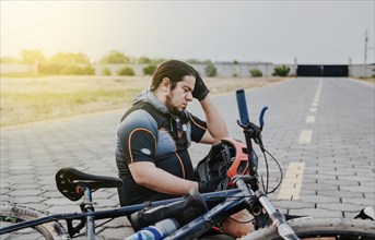 Male cyclist sitting with headache. Cyclist on the pavement with a headache. Concept of cyclist