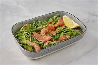 A vibrant salad features fresh smoked salmon slices mixed with crisp arugula and cucumber,