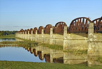 Close-up of stone bridge pillars and the calm water below reflecting the bridge on a clear day,