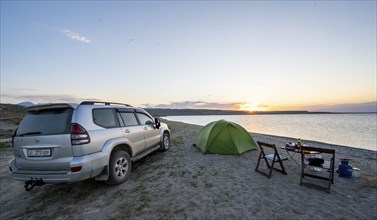 Camping on the lakeshore, off-road vehicle next to tent and camping chairs, sunset at Issyk Kul