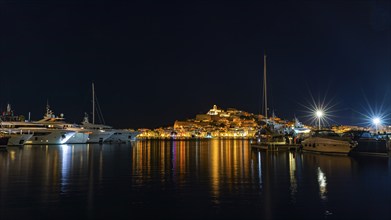 Luxury yachts anchoring in the harbour, behind the illuminated fortress and the old town, night