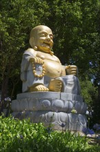 Golden seated Buddha statue in the greenery, surrounded by flowers and trees, radiates peace and