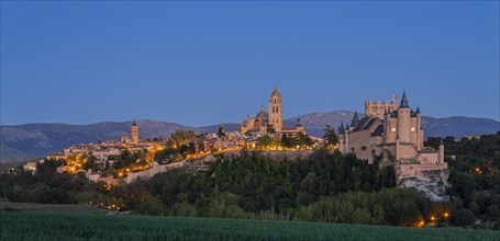 Night scene with an illuminated castle and city in front of dark mountains, a calm and peaceful