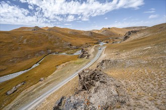 Car on road through mountain valley with hills with yellow grass, Naryn province, Kyrgyzstan, Asia