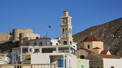 Church tower and surrounding buildings with Greek flag under clear sky, Colourful mountain village,