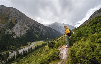 Mountaineer on a rock, Green mountain valley with river and steep mountain peaks, Chong Kyzyl Suu