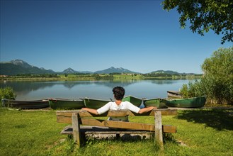 Woman sitting relaxed on a bench, Hopfensee, near Fuessen, Ostallgaeu, Allgaeu, Bavaria, Germany,