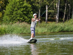 Young man with wakeboard in lake, water sports, water skiing in wakepark