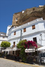 White buildings and restaurant in Setenil de las Bodegas under rocks, blue sky, cave dwellings,