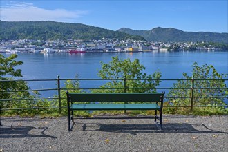 A green bench stands in front of a railing with a view of the city by the water and the surrounding