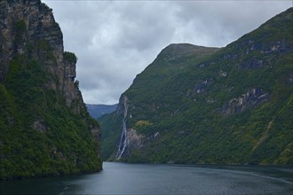 A fjord surrounded by rocky mountains under a cloudy sky with a waterfall in the background,